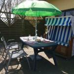 Terrasse mit Tisch, Stühlen und grünem Sonnenschirm neben Strandkorb.