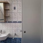 Badezimmer mit Waschbecken, Spiegel und Holzregalen an der Wand.