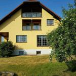 Gelbes Haus mit Balkonen und Garten. Außenbeleuchtung sichtbar.