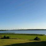 Weitläufiger Blick auf einen See mit grünen Wiesen und Bäumen am Ufer.