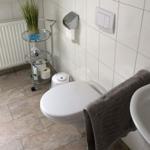 Badezimmer mit Toilette, Waschbecken und Duschbereich. Fliesenboden und weiße Wände.
