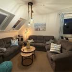 Wohnzimmer mit drei Sofas, runden Tischen und Dachfenstern. Wandbild zeigt Strand.