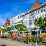 Streifenmarkise, Tische und Stühle vor einem Gebäude mit rotem Dach und Fenstern.