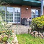 Terrasse mit Tisch und Stühlen, umgeben von Grünflächen und Blumen.