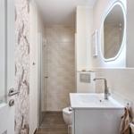 Badezimmer mit Dusche, Waschbecken und Toilette. Wand mit Tapete und beleuchtetem Spiegel.