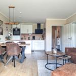 Wohnküche mit Esstisch, Sofa und Küchenzeile. Holzboden und Wandbild sichtbar.