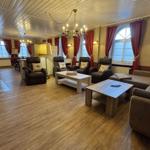 Großes Wohnzimmer mit Sitzgelegenheiten, Holzboden und Fenstern mit roten Vorhängen.