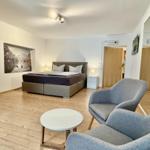 Schlafzimmer mit Bett, Sessel und Wandbild. Holzboden und Deckenleuchten.