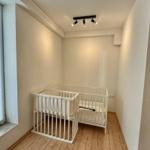 Kinderzimmer mit weißem Babybett und Holzboden. Fenster mit Jalousie.