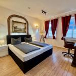 Schlafzimmer mit Doppelbett, Schreibtisch, roten Vorhängen und Holzboden.