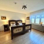 Schlafzimmer mit Doppelbett, zwei Nachttischen und Fenster mit Jalousien.