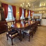 Esszimmer mit Holztisch, Stühlen und roten Vorhängen an den Fenstern.