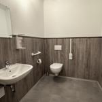 Badezimmer mit Toilette, Waschbecken und Spiegel an Holzwandverkleidung.