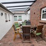 Terrasse mit Tisch und Stühlen unter Dach, beiderseits Hauswände.