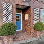 Eingang mit blauer Tür, rotem Backsteinhaus und weißen Gitterelementen.