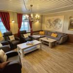 Wohnzimmer mit Sofa, Sesseln, Tisch und Wandkarte.