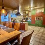 Küche mit Essbereich, grün-rot lackierten Schränken und Holztisch mit Stühlen.