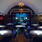Großer Saal mit runden Tischen, Bühne und Kronleuchter.