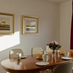 Esstisch mit Stühlen, Tassen, Teller und Blumenarrangement an der Wand.