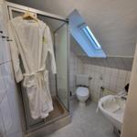 Badezimmer mit Dusche, Toilette und Waschbecken. Bademantel hängt an der Dusche.