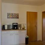 Küche mit Arbeitsplatte, Kaffeemaschine und Mikrowelle. Holztür und Wandbild sichtbar.