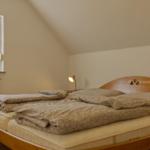 Schlafzimmer mit Doppelbett, Holzkopfteil und Fenster mit Vorhängen.