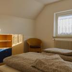 Ein Schlafzimmer mit Doppelbett, Schrank und Stuhl neben dem Fenster.