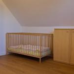 Kinderzimmer mit Holzkrippe, Kleiderschrank und Holzboden unter schräger Decke.