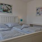 Schlafzimmer mit weißem Bett, zwei Bildern an der Wand und einer Nachttischlampe.