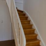 Holzgetreppe mit weißer Balustrade führt zur oberen Etage. Links ist eine Tür zum Wohnbereich.