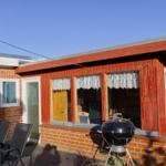 Roter Holzsaal mit Fenstern und Grill auf Terrasse. Neben einem Backsteinhaus.