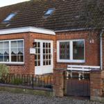 Rotes Backsteingebäude mit weißer Tür und Fenstern, Dach mit Dachfenstern, kleine Vorgärtnereingang.