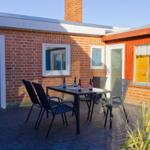 Terrasse mit Tisch und Stühlen vor rotem Backsteinhaus mit Fenstern und Tür.