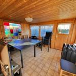 Helle Holzvertäfelung, große Fenster, Tisch mit Stühlen, Grill und Tür