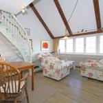 Living and dining area with wooden floors, floral chairs, and staircase.