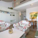 Living and dining area with floral chairs, white cabinets, and staircase to gallery.