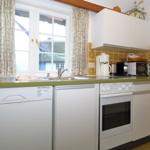 Kitchen with sink, faucet, stove, and oven. Window with curtains and yellow tiles.