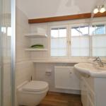 Bathroom with shower, toilet, and sink under window.