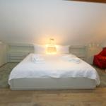 Bedroom with sloped ceilings, white bed, and red armchairs.