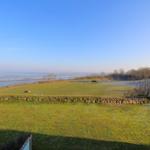 Large green area with view of the water and a stone wall in the foreground.