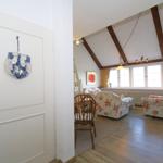 Entrance with door and view into living room with wooden beams and floral chairs.