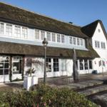 Holiday home with thatched roof and white windows. Front garden with plants and stone steps.