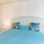 Ein Schlafzimmer mit weißem Bett und blauer Bettwäsche. An den Wänden hängen zwei Nachttische mit Lampen.