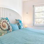 Schlafzimmer mit Bett, Kissen und Fenster. Blaue Bettwäsche und Wanddekoration.