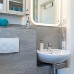 Badezimmer mit Waschbecken, Spiegel und Toilette. Aufgehängt sind Handtücher und ein Leuchtturm-Objekt.