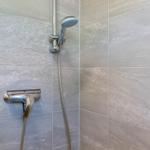 Duschbereich mit Handbrause und Wandhahn an grauen Fliesen