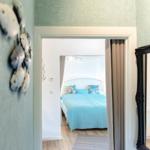 Schlafzimmer mit blauem Bett und Fensterblick. Wanddekoration und Spiegel sichtbar.