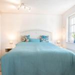 Schlafzimmer mit Bett, Nachttischen und Fenster. Blaue Bettwäsche und weiße Möbel.