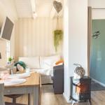 Wohnzimmer mit Sofa, Esstisch und Kaminofen. Wand mit Streifenmuster und Pflanzen.