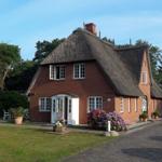 Red brick house with thatched roof, white windows, and flower beds near the entrance.